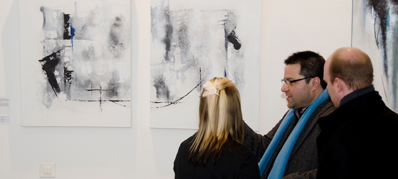 Gäste und Künstlerin bei Kunstausstellung mit abstrakten Werken im Hintergrund